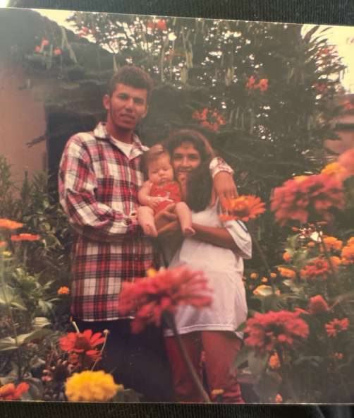 Helena Maria com o marido e a filha Eduarda bebê, no quintal cheio de flores