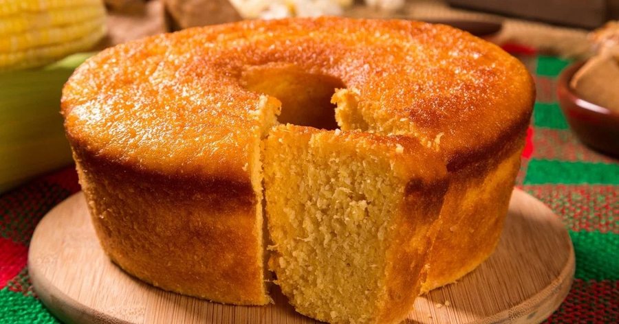 Bolo de fubá dourado em forma de furo, com uma fatia cortada